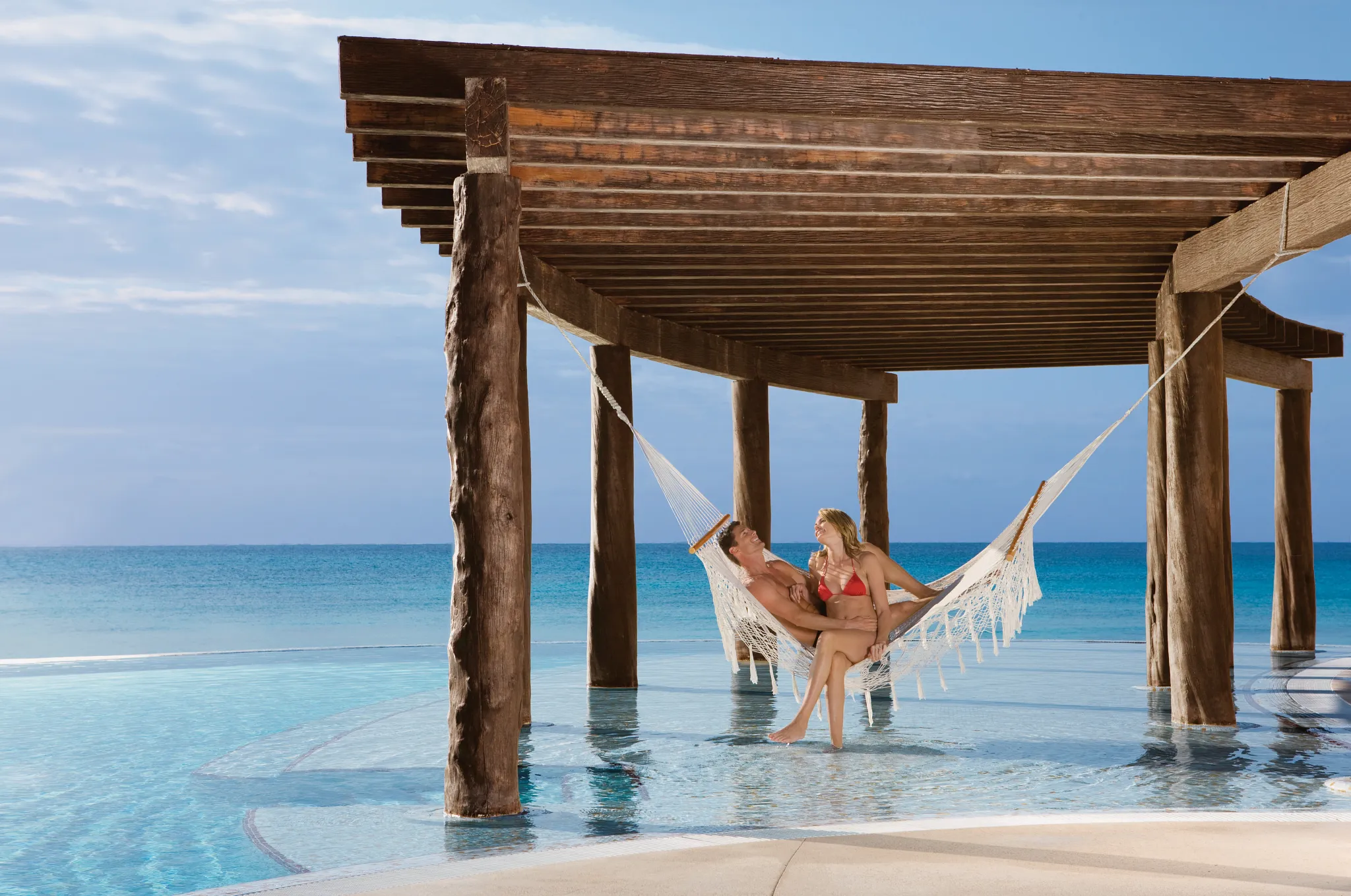 Couple relaxing in a hammock over the infinity pool at Dreams Jade Resort & Spa.