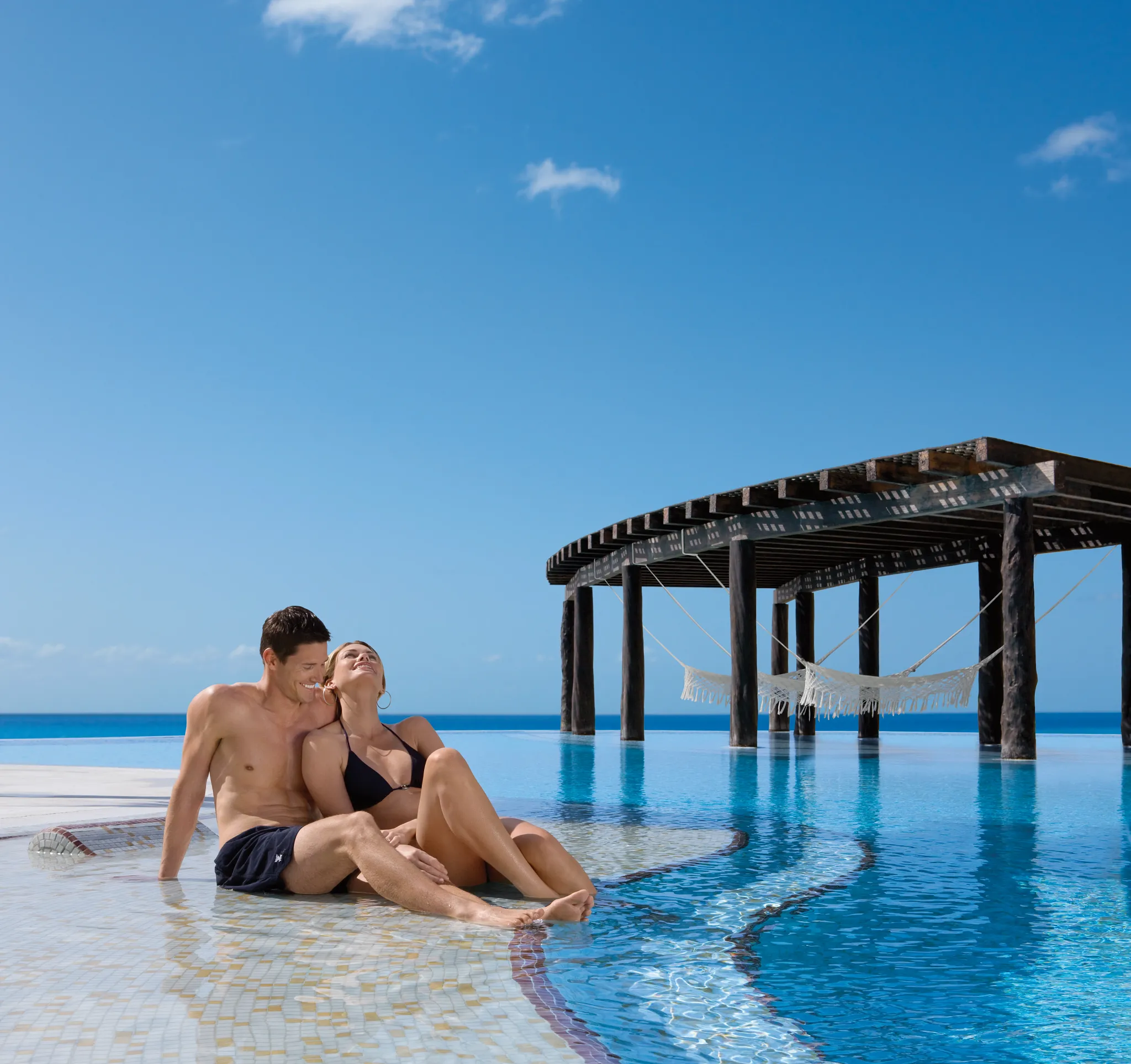 Couple relaxing at the infinity pool with ocean views at Dreams Jade Resort & Spa.